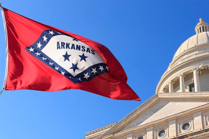 State flag of Arkansas flowing in the wind in front of the state’s capitol building.