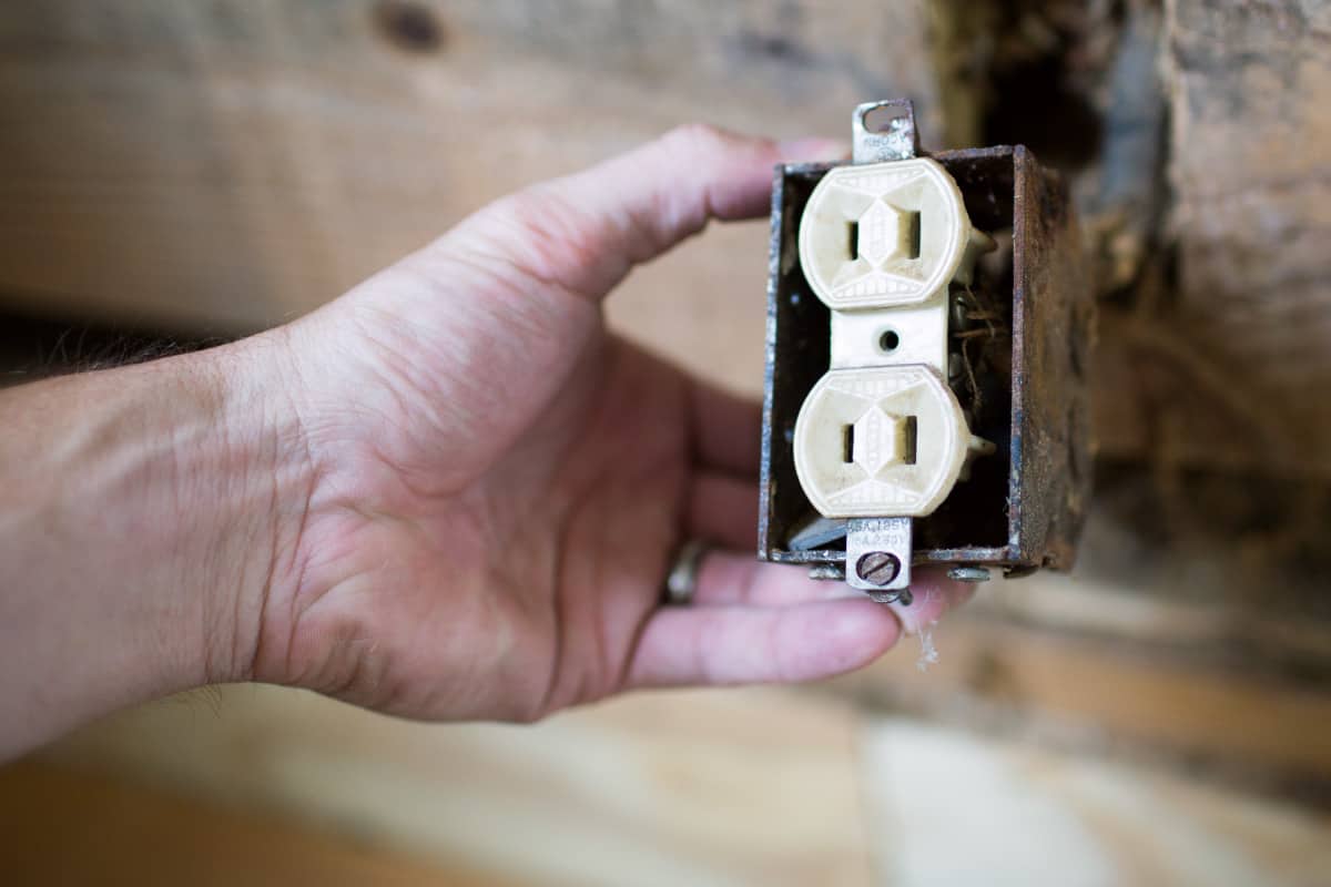 A man holding an exposed wall outlet.