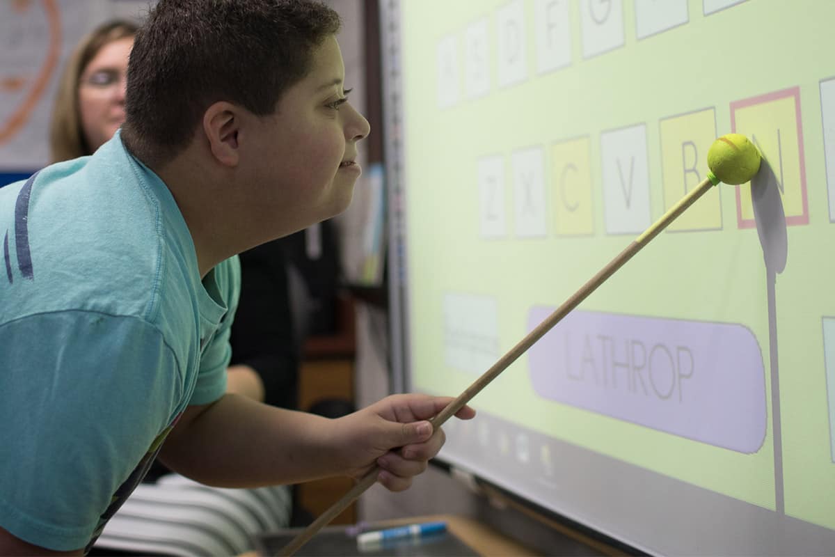 Student pointing to a letter being displayed from a projector.