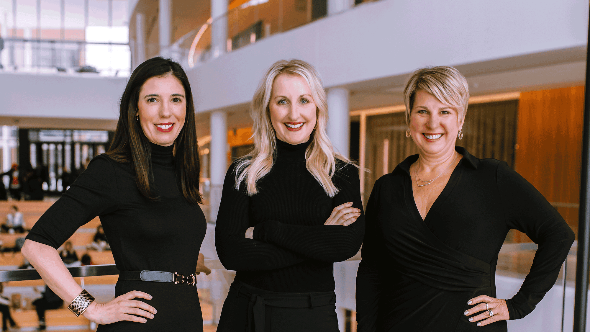 three women, all wearing black standing side by side in a business setting.