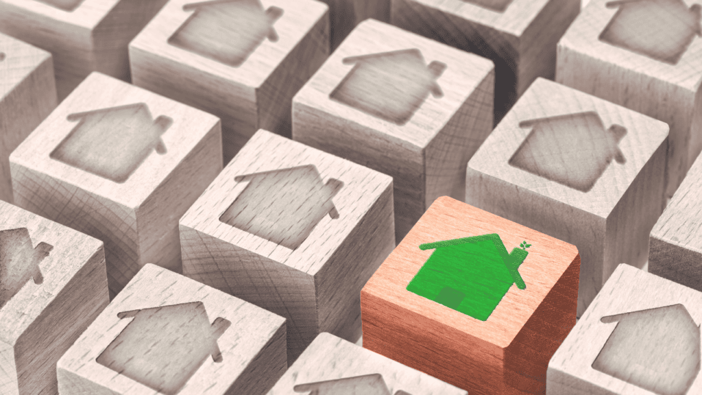 rows of brown wooden blocks with an outline of a house etched in each block with one block a lighter color brown and a green house on it.